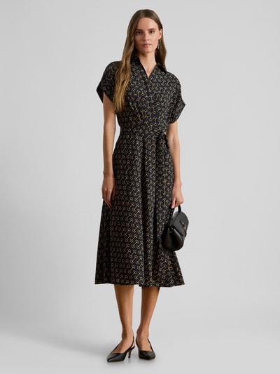 Frauenmodel trägt Tailliertes Wickelkleid aus Chiffon von Lauren Ralph Lauren mit Allover-Muster in Schwarz und Beige, Midi-Länge, V-Ausschnitt, kurzarm, Taillengürtel, lockerer Chiffonstoff, Ganzkörperansicht von vorne.