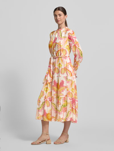 Frauenmodel trägt Regular Fit Midikleid aus reiner Viskose mit Stehkragen von HERZENS, floraler Allover-Print, Strukturmuster, taillierte Passform, abnehmbares Stoffband, farbenfrohe Töne in Rosa, Gelb und Grün, langärmeliges Design, leicht glänzende Textur, Ganzkörperansicht von vorne.