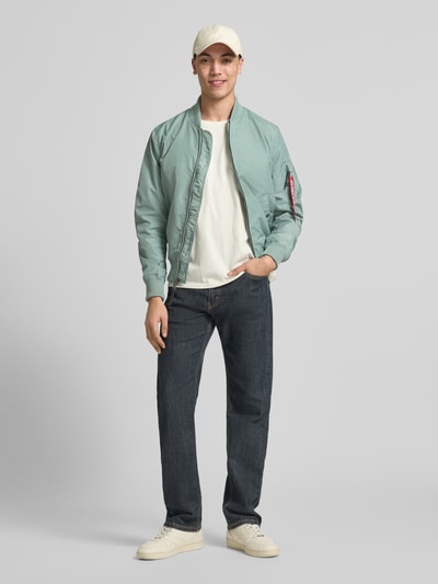 Männermodel trägt mintgrüne Regular Fit Jacke mit Stehkragen von Alpha Industries, Armtasche, Eingrifftaschen, Reißverschluss, elastische Abschlüsse, Rückenlänge 66 cm, Schulterbreite 48 cm, Brustweite 54 cm, Ärmellänge 68 cm, Ganzkörperansicht von vorne.