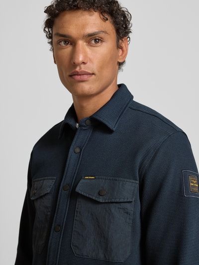 Männermodel trägt Regular Fit Hemdjacke mit Brusttaschen von PME Legend, dunkelblauer Baumwoll-Mix mit Stretch-Anteil, Strukturmuster, Kentkragen, Label-Details, Knopfleiste, Nahaufnahme Oberkörper.
