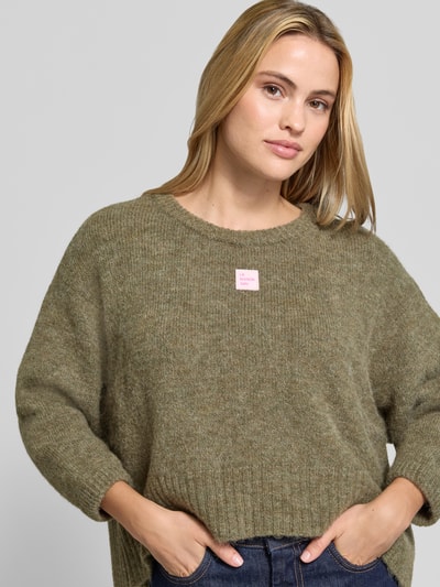 Frauenmodel trägt Oversized Pullover mit Alpaka-Anteil Modell 'East' von American Vintage, Strick-Optik, Logo-Patch, Nahaufnahme Oberkörper.