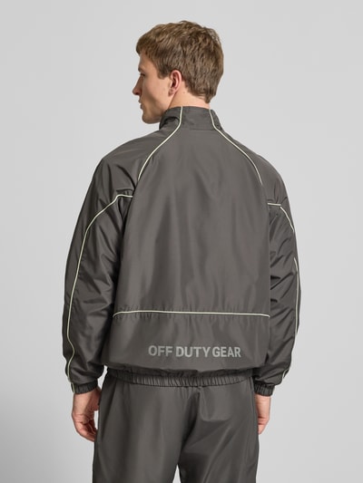 Männermodel trägt Trainingsjacke mit Reißverschlusstaschen von HALO in Grau, Regular Fit, Stehkragen, Label-Print, Rückenlänge 70 cm, Ärmellänge 72 cm, Ganzkörperansicht Rückansicht.