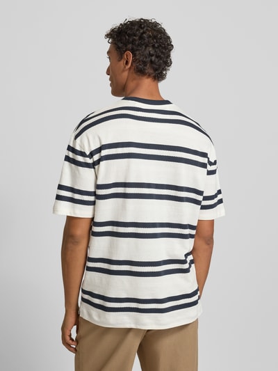 Männermodel trägt T-Shirt mit Label-Detail von Guess, weiße Baumwolle, navy Streifen, lockerer Schnitt, Rückenlänge 71 cm, Ganzkörperansicht Rückansicht.