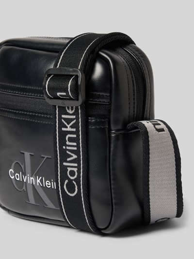 Produktfoto, schwarze Herren Umhängetasche mit Logo-Prägung von CK Calvin Klein, dezente Glanzoptik und Stoffriemen auf grauem Hintergrund