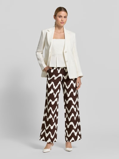 Kobiece model prezentuje spodnie z szerokimi nogawkami Wide Leg Pants aus Viskose-Mix mit elastischem Bund od OPUS PANTS, mieszanka wiskozy z lnem, krój loose fit, model 'Malotta', szerokość w rozmiarze 36: 37 cm, długość wewnętrzna nogawki 79 cm, brązowo-biały wzór zygzak, tekstura gładka, widok całej sylwetki z przodu.
