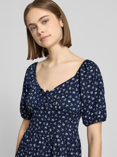 Frauenmodel trägt Minikleid mit Puffärmeln Modell 'HILLARY' von Only, dunkelblau mit floralem Allover-Muster aus Crêpe, taillierte Passform, Schleifenapplikation, Karree-Ausschnitt, Nahaufnahme Oberkörper.