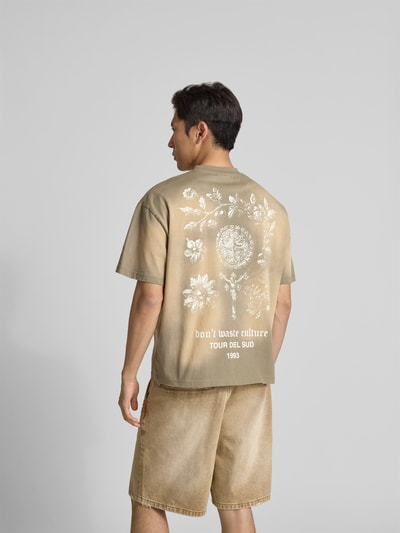 Männermodel trägt T-Shirt mit Label-Print von Don’t Waste Culture in Beige mit floralen Weiß-Prints, reine Baumwolle, Rückansicht, Ganzkörperansicht.
