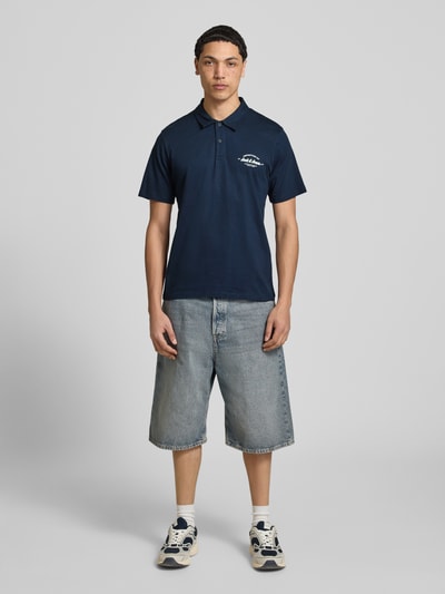 Männermodel trägt donkerblauw poloshirt met labelprint van puur katoen, regular fit, model 'BRANDON' van Jack & Jones, polokraag, korte knoopsluiting, ruglengte bij maat M 71 cm, Ganzkörperansicht von vorne.