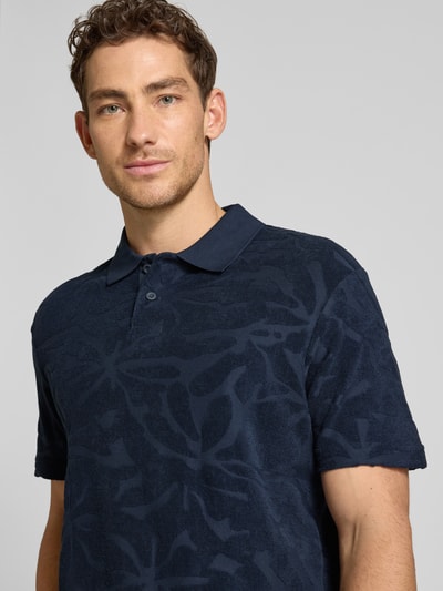 Männermodel trägt Regular Fit Poloshirt aus Baumwoll-Mix Modell 'PE_FLOWER' von BOSS Orange in Dunkelblau mit Allover-Muster, Nahaufnahme Oberkörper.