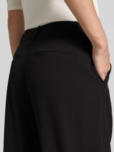 Frauenmodel trägt Stoffhose mit französischen Eingrifftaschen Modell 'DANTA' von b.young, schwarzer Material-Mix, Detailaufnahme Rücken, Barrel Fit, Bund und Gesäßleistentaschen sichtbar, Kontext: Damenhose mit Biesen, Haken- und Reißverschluss, Bundweite 40 cm, Innenbeinlänge 73 cm.