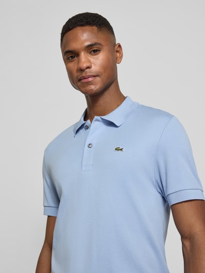 Männermodel trägt Regular Fit Poloshirt aus reiner Baumwolle von Lacoste in Hellblau mit Logo-Detail, Nahaufnahme Oberkörper