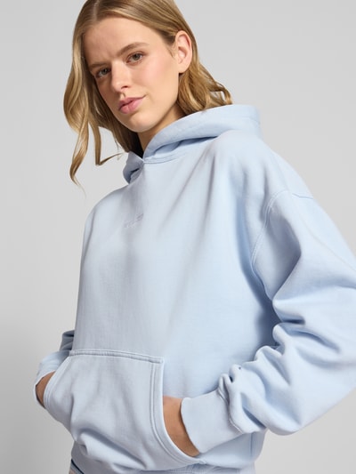 Frauenmodel trägt Oversized Hoodie mit Logo-Stitching Modell 'CLARITA' von Pegador in Hellblau, Baumwoll-Mix, Känguru-Tasche, Nahaufnahme Oberkörper.