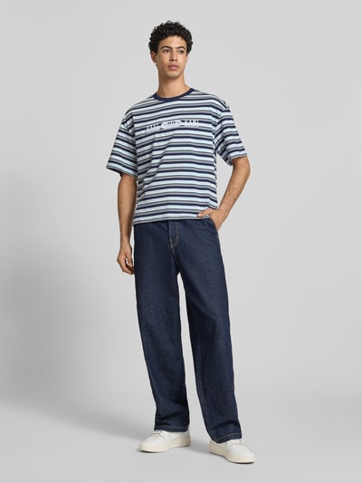 Männermodel trägt Regular Fit T-Shirt mit Logo-Stitching von KARL KANI, gestreift in Blau und Weiß, Reine Baumwolle, Ganzkörperansicht von vorne.
