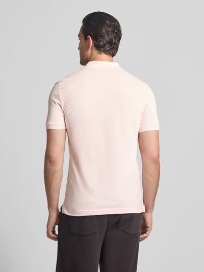 Męski model nosi Slim Fit Poloshirt aus reiner Baumwolle od Lacoste, jednolity kolor, krój slim fit, wyhaftowane logo, kołnierzyk polo, krótki rękaw, zakończenie rękawów prążkowane, dół z rozcięciami po bokach, wykończenie z piki, czysta bawełna, całkowity widok z tyłu.