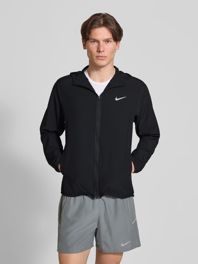 Männermodel trägt schwarze Trainingsjacke mit Logo-Print und Stehkragen von NIKE TRAINING, gerader Schnitt, Reißverschluss, seitliche Eingrifftaschen, elastische Ärmelabschlüsse; Rückseite 69 cm, Ärmellänge 65 cm bei Größe M, Ganzkörperansicht von vorne.