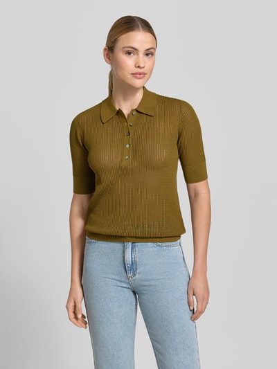 Frauenmodel trägt Lochstrick-Poloshirt - curated by Mary Braun von Style Icon Collection in semitransparenter Strick-Optik, Slim-Fit, Polokragen, Kurzärmelig, Rückenlänge bei Größe S 57 cm, Ärmellänge 27 cm, olivefarbener Ton, strukturierte Oberfläche, Ganzkörperansicht von vorne.