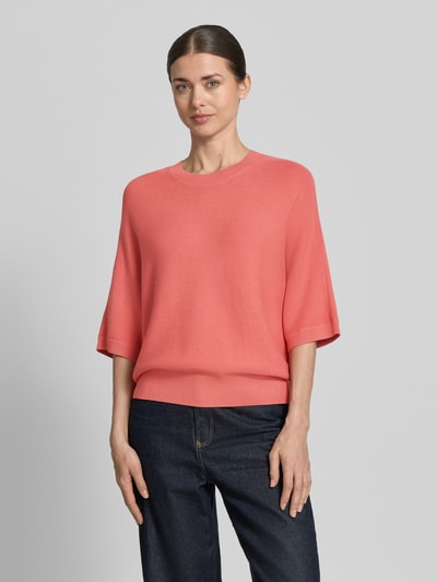 Modelka kobieca nosi Strickpullover aus Viskose-Mix mit Rundhalsausschnitt od MSCH Copenhagen, kolor koralowy, krój loose fit, 3/4-rękawy, prążkowany dekolt, prążkowane wykończenia, długość tyłu 51 cm, długość rękawa 35 cm, widok całej sylwetki z przodu.