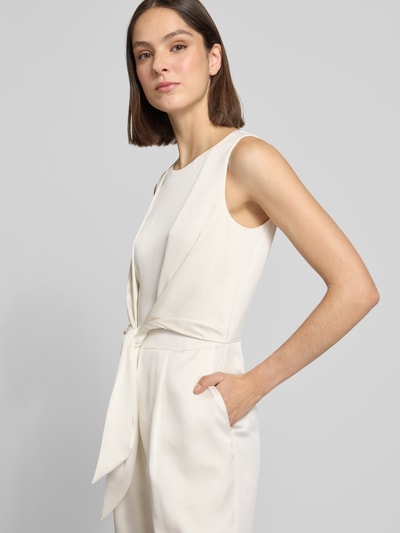 Modelka nosi Jumpsuit aus Satin mit Bindegürtel von Christian Berg Cocktail, kolor jasny kremowy, gładka faktura, lekko taliowany krój, okrągły dekolt, pasek w talii, zamek z tyłu, prosta nogawka, długość pleców w rozmiarze 36: 42 cm, szerokość w rozmiarze 36: 42 cm, całkowita długość: 155 cm, długość nogawki wewnętrznej: 81 cm, zbliżenie na górną część ciała