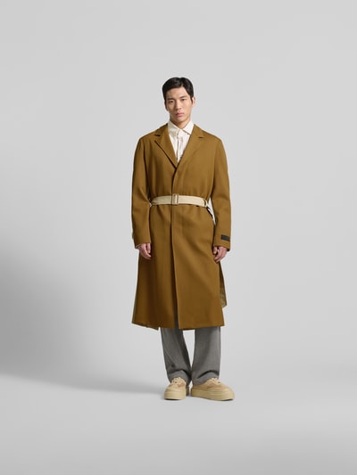 Männermodel trägt Mantel aus reiner Schurwolle von MM6 Maison Margiela in Braun mit Reverskragen und Taillengürtel, Ganzkörperansicht von vorne.
