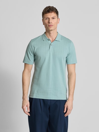 Männermodel trägt Regular Fit Poloshirt aus reiner Baumwolle von Marc O'Polo in Hellgrün mit Gitterkaro Struktur und Polokragen, Ganzkörperansicht von vorne.