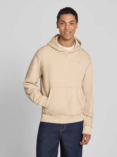 Männermodel trägt Regular Fit Hoodie aus reiner Baumwolle von G-Star RAW in Beige, kombiniert mit blauer Jeans, Ganzkörperansicht von vorne.