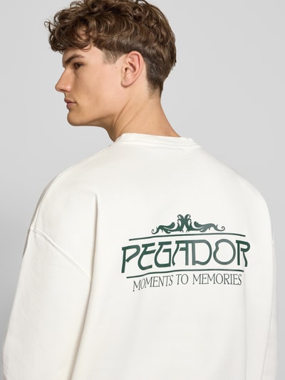 Mężczyznamodel nosi Oversized Sweatshirt mit Logo-Print Modell 'Stavoren' od Pegador z mieszanki bawełny, okrągły dekolt, krój oversized fit, nadruk z logo, elastyczne wykończenia, długość tyłu 70 cm, długość rękawów 65 cm, jasny kolor, gładka faktura, detailaufnahme tyłu.