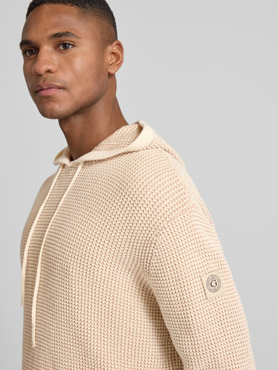 Männermodel trägt Slim Fit Hoodie mit Viskose-Anteil Modell 'Kem' von Guess, Strick-Optik, beige, Nahaufnahme Oberkörper.