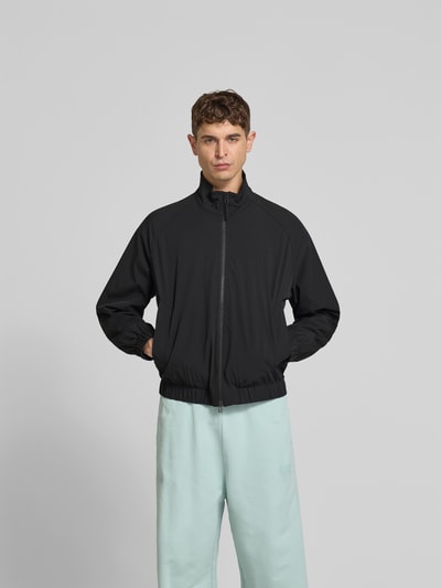 Männermodel trägt Blouson mit Stretch-Anteil von Forét in Schwarz, Elastischer-Material-Mix, Zweiwege-Reißverschluss, Eingrifftaschen, Lockere Passform, Ganzkörperansicht von vorne.