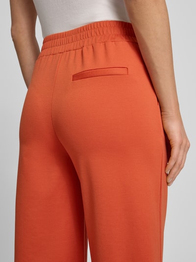 Vrouwenmodel draagt Wide Fit Stoffhose met Viskose-Anteil Modell 'Kate' van ICHI in oranje, zicht op achterzijde, detailopname. Elastische tailleband, achterzak, zachte textuur.