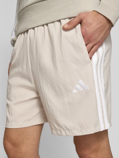 Männermodel trägt Regular Fit Sport-Shorts mit Kontraststreifen von adidas Sportswear, unifarben, seitliche Eingrifftaschen, Nahaufnahme Oberschenkel.
