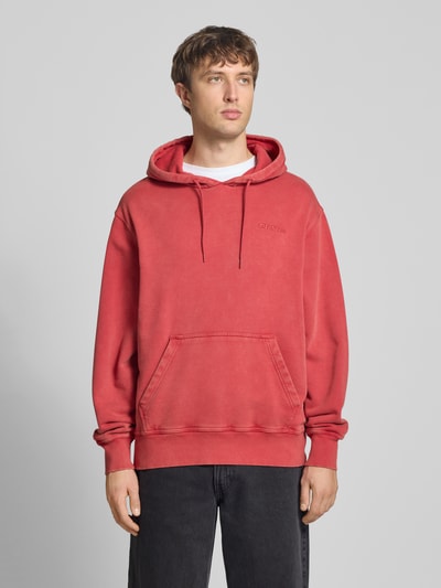 Männermodel trägt roten Hoodie mit Label-Stitching und Känguru-Tasche von Dickies, Relaxed Fit, Baumwoll-Mix, Ganzkörperansicht von vorne