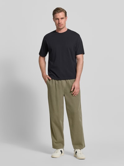 Männermodel trägt Jog Pants mit französischen Eingrifftaschen Modell 'LYCAZ' von American Vintage in Olivgrün, Straight Fit, reine Baumwolle, elastischer Bund, Ganzkörperansicht von vorne.
