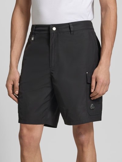 Männermodel trägt Regular Fit Shorts mit Cargo-Taschen von Moose Knuckles in Schwarz, mit Logo-Detail und Eingrifftaschen, Nahaufnahme Oberkörper.
