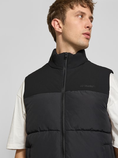 Männermodel trägt Weste mit Stehkragen Modell 'RAZE' von JACK & JONES, Schwarz mit Label-Print, Reißverschluss, Nahaufnahme Oberkörper.