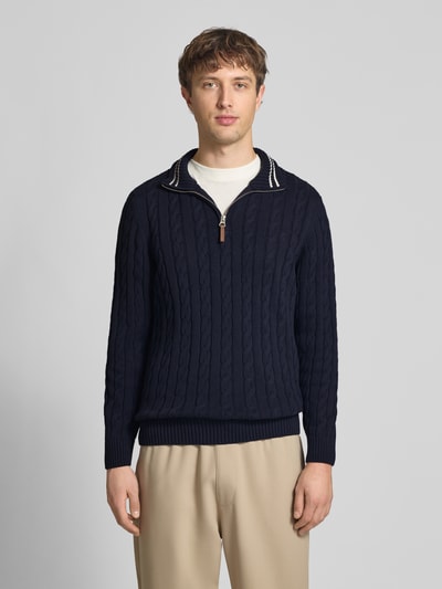 Männermodel trägt Strickpullover aus reiner Baumwolle von Superdry in Dunkelblau mit Zopfmuster, enger Passform, Ganzkörperansicht von vorne.