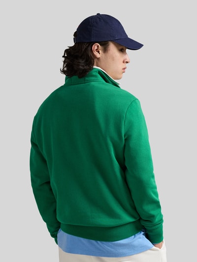 Männermodel trägt Relaxed Fit Troyer aus Baumwoll-Mix von Polo Ralph Lauren in Unigrün mit gerippten Abschlüssen und Reißverschluss, Ganzkörperansicht Rückansicht.