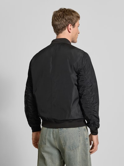 Männermodel trägt Regular Fit Bluzon mit college-kołnierzem Model 'JOSHUA' von Only & Sons, jednolity kolor, krój regular fit, zamek błyskawiczny, długi rękaw, prążkowane zakończenia, wpuszczane kieszenie boczne, kieszeń na rękawie z zamkiem, widok całej sylwetki z tyłu.
