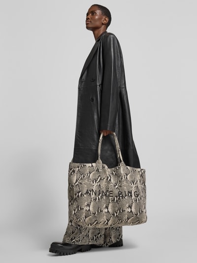 Frauenmodel trägt Shopper aus reiner Baumwolle von Anine Bing mit Label-Print, Strukturmuster, kurzem Tragehenkel, offene Hauptfach, Grau-Schwarz-Töne, Ganzkörperansicht von vorne.