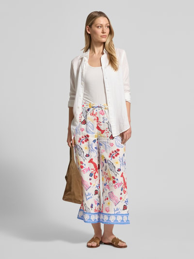 Frauenmodel trägt Wide Fit Leinenhose mit Allover-Motiv-Print von Christian Berg Woman; bunt gemustert, elastischer Bund, lockere Passform, Motivdetails und Blautöne, reine Leinen-Textur, Ganzkörperansicht von vorne.