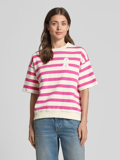 Frauenmodel trägt Oversized Fit Sweatshirt aus reiner Bio-Baumwolle Modell 'BAMIKAA' von Armedangels mit pink-weißen Streifen, Logo-Stitching, Rundhalsausschnitt und kurzen Ärmeln, Sweat-Textur, Allover-Muster, Nahaufnahme Oberkörper.