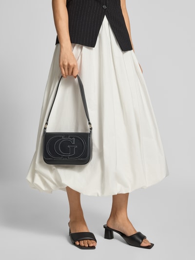 Frauenmodel trägt Shoulder Bag mit Logo-Detail Modell 'Ruby' von GUESS, schwarzes Leder, silberfarbene Details, Hauptfach mit Überschlag, Nahaufnahme Unterkörper.