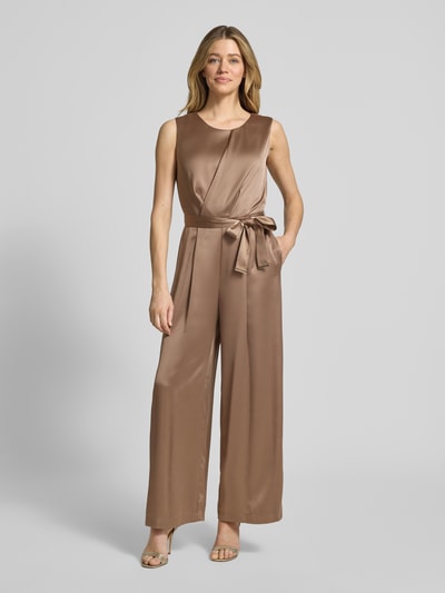 Frauenmodel trägt Shaped Fit Jumpsuit mit Taillengürtel zum Binden von s.Oliver BLACK LABEL in unifarbenem, glänzendem Satin, Ganzkörperansicht von vorne.