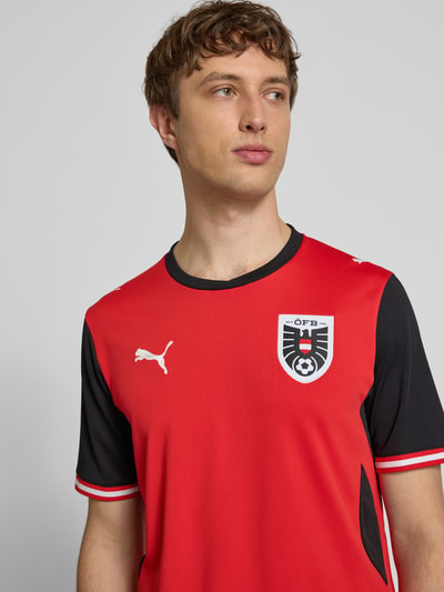 Männermodel trägt Österreich Heimtrikot 2026 von PUMA, Herren Trikot-Look, Gerader-Schnitt, Rundhalsausschnitt, Logo-Print, Patch, Modell 'ÖFB Home', Rückenlänge 72 cm bei Größe M, Nahaufnahme Oberkörper.