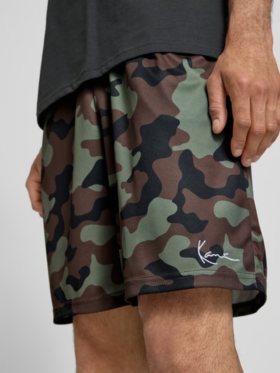 Männermodel trägt Regular Fit Shorts mit elastischem Bund von KARL KANI, Camouflage-Strukturmuster, Logo-Stitching, Nahaufnahme Oberschenkel.