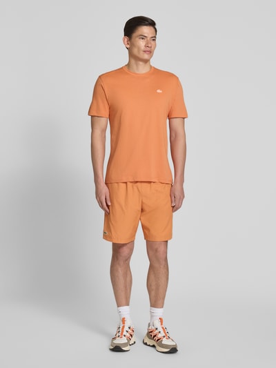 Mannenmodel draagt Relaxed Fit Sport-Shorts met Logo-Stitching van Lacoste Sport in effen oranje, elastische tailleband, zijzakken, tunnelkoord, relaxed fit, volledige lichaamsvoorzijde.