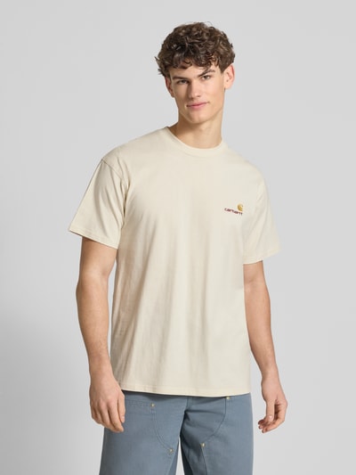 Männermodel trägt T-Shirt mit Label-Stitching und Rundhalsausschnitt von Carhartt Work In Progress, cremefarben, Regular Fit, Ganzkörperansicht von vorne.