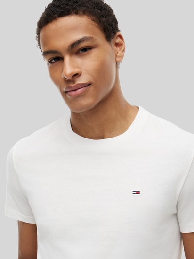 Męskimodel nosi Slim Fit T-Shirts aus reiner Baumwolle im 2er-Pack von Tommy Jeans, kolor biały, krój slim fit, okrągły dekolt, krótki rękaw, wyhaftowane logo, materiał: bawełna, zestaw 2 szt., Nahaufnahme górnej części ciała.