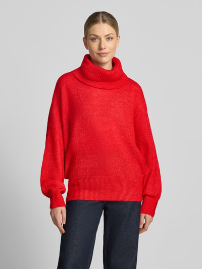 Frauenmodel trägt Relaxed Fit Strickpullover mit Rollkragen Modell 'IHKAMARA' von ICHI in leuchtendem Rot, strukturierte Textur, Ganzkörperansicht von vorne, Material-Mix mit Alpaka-Anteil, elastische Abschlüsse, Rückenlänge 63 cm, Ärmellänge 72 cm.