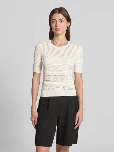 Frauenmodel trägt T-Shirt in Strick-Optik mit Rundhalsausschnitt von Guess in Creme, gerippte Abschlüsse, körpernaher Schnitt, Ganzkörperansicht von vorne.