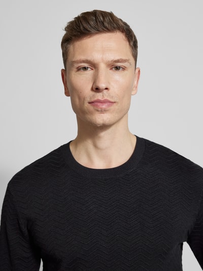 Männermodel trägt Strickpullover aus Viskose-Mix von ARMANI EXCHANGE in Schwarz, Rundhalsausschnitt, strukturierte Strick-Optik, Nahaufnahme Oberkörper.